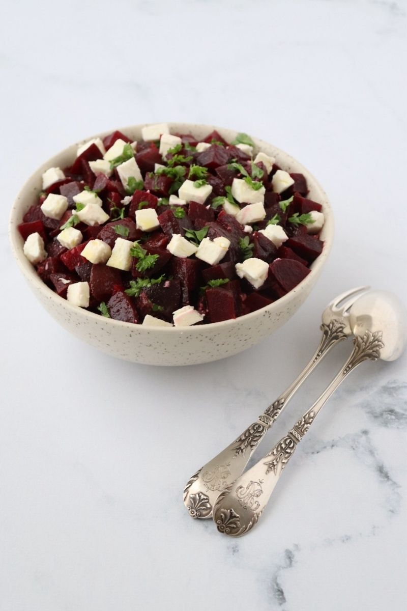 beetroot and feta cut in cubes in a large bowl with chopped parsley on top a fork and a spoon on the side