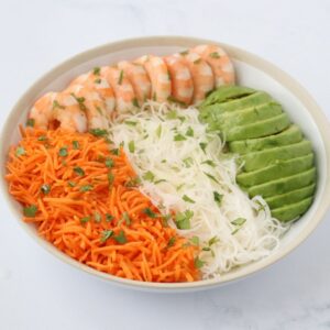 a bowl filled with vermicelli, grated carrots, shrimp and avocado garnished with chopped cilantro
