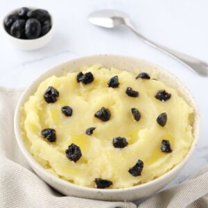 a bowl full of mashed potatoes topped with pieces of black olives, a small bowl of black olives in the background