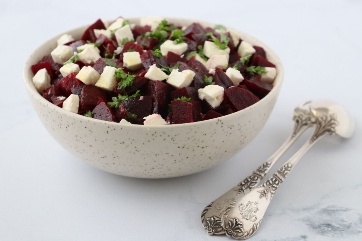beetroot and feta cut in cubes in a large bowl with chopped parsley on top a fork and a spoon on the side