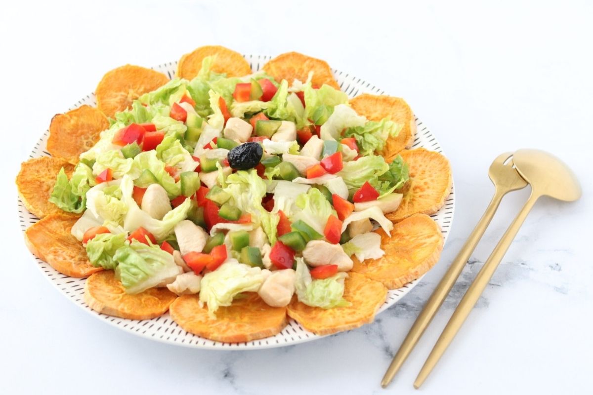 a colorful salad with sweet potato slices, lettuce, chicken, red bell pepper, green bell pepper and a black olive in the center