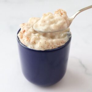 a blue cup full of dairy free rice pudding srpinkled with cinnamon powder and a spoon taking out a spoonful
