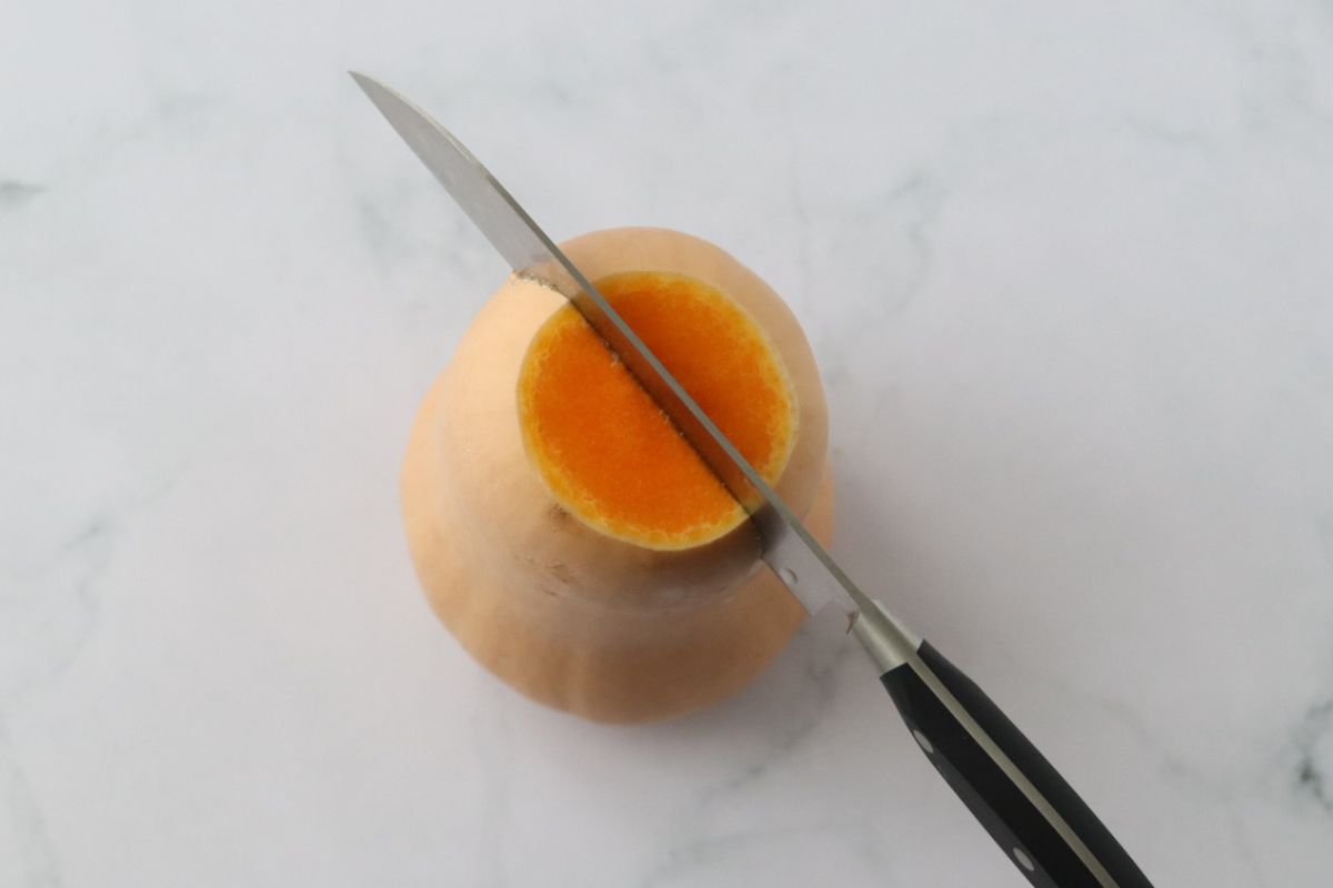 a butternut sqaush being cut length wise with a large knife