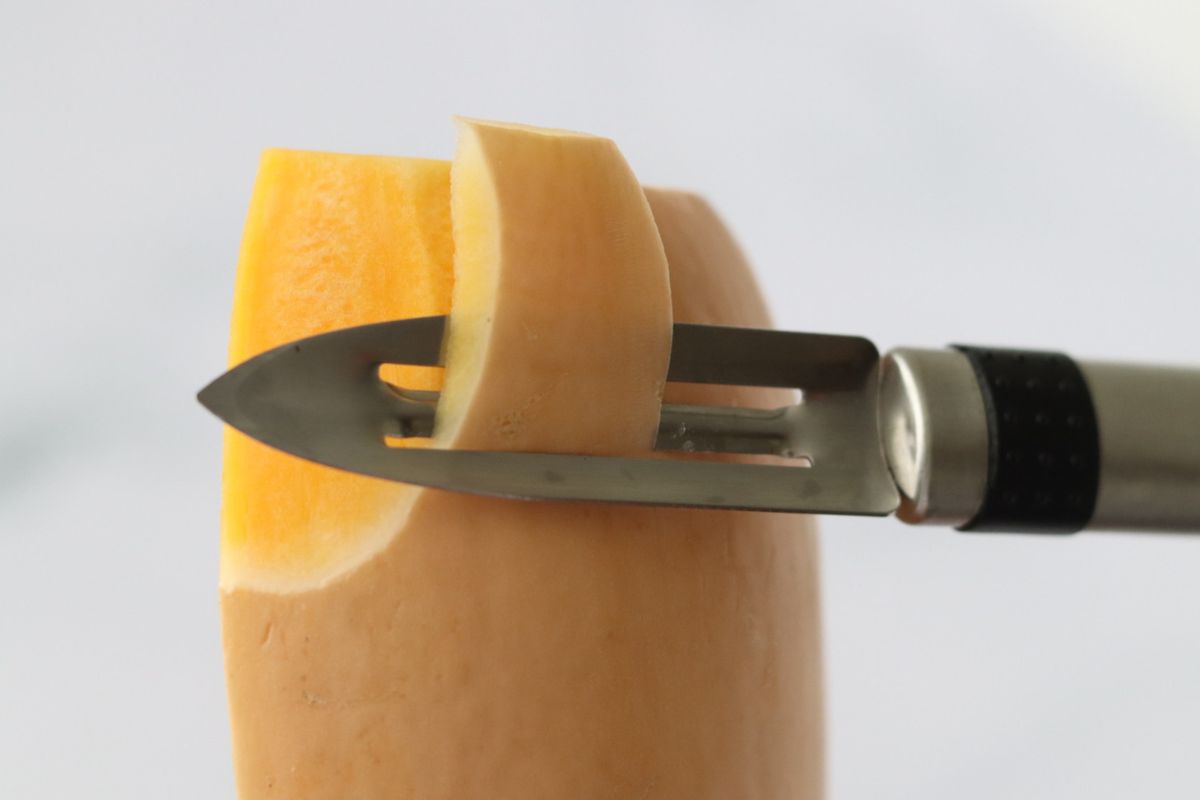 a butternut squash being peeled with a peeler knife