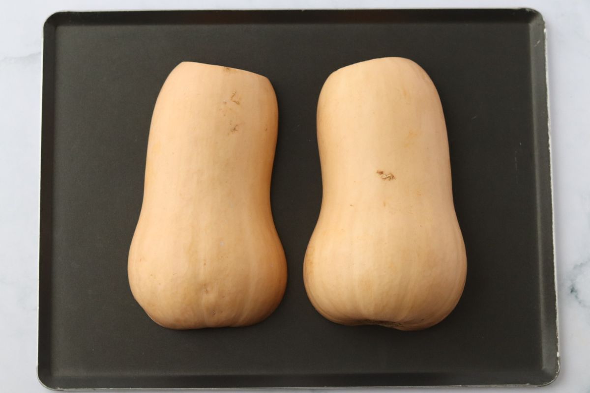 2 halves of a butternut squash cut side down on a baking tray