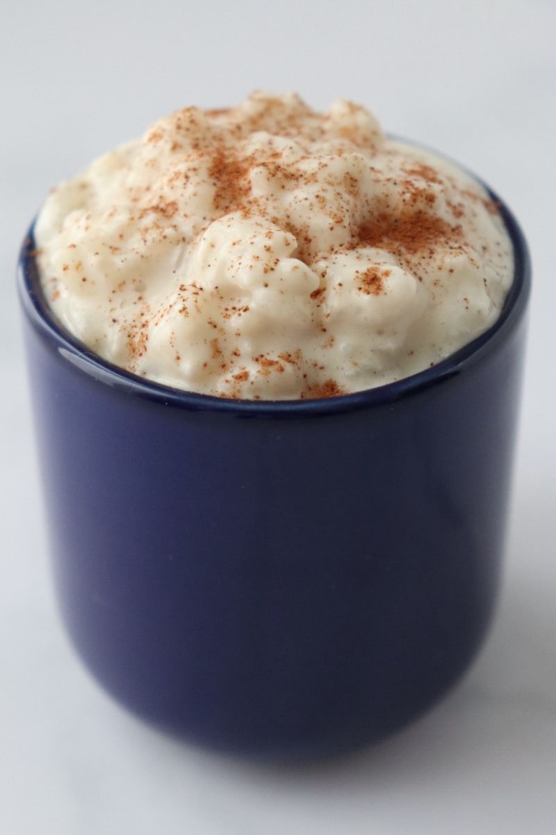 a blue cup full of dairy free rice pudding srpinkled with cinnamon powder