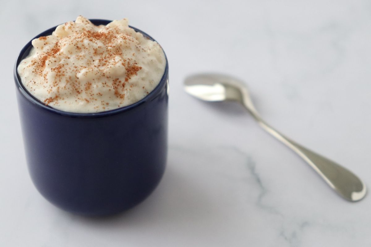 a blue cup full of dairy free rice pudding srpinkled with cinnamon powder
