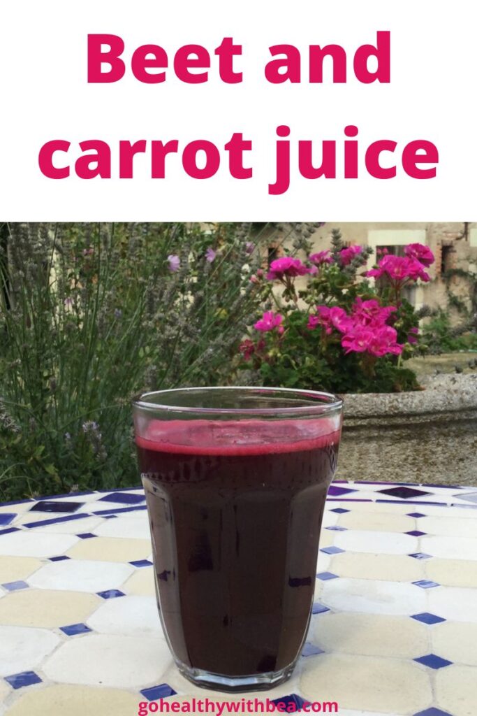 a glass of beet and carrot juice on a table in a garden with flowers in the background
