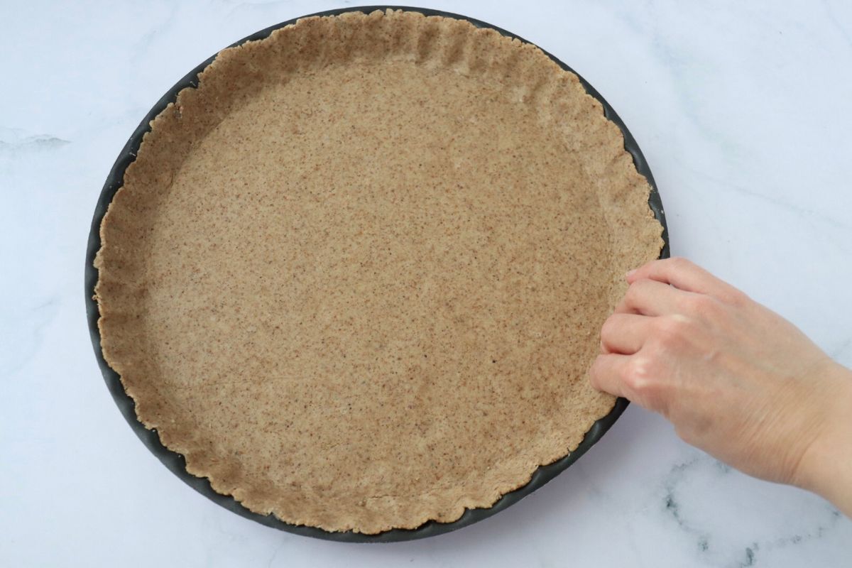a hand pressing the pie crust on the sides of the pie tin