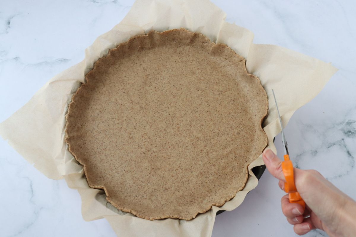 someone cutting the excess of parchment paper to fit the pie tin