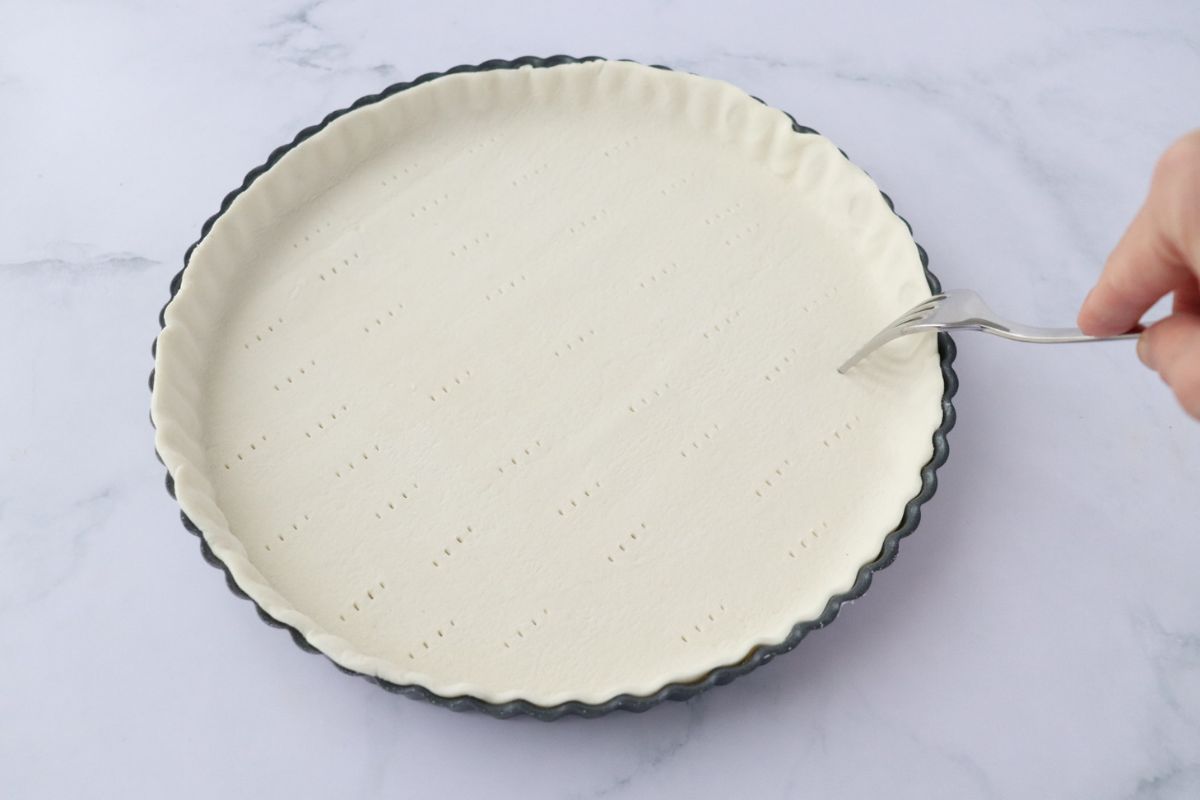 picture of a pie crust in a pie pan being pricked with a fork
