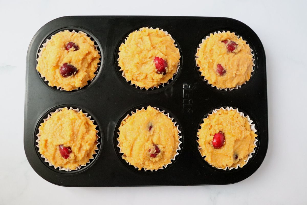 a 6 cup muffin pan filled with orange cranberry muffin batter