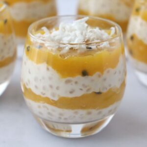 a glass full of layered mango tapioca pudding topped with grated coconut and 4 other glasses in the background
