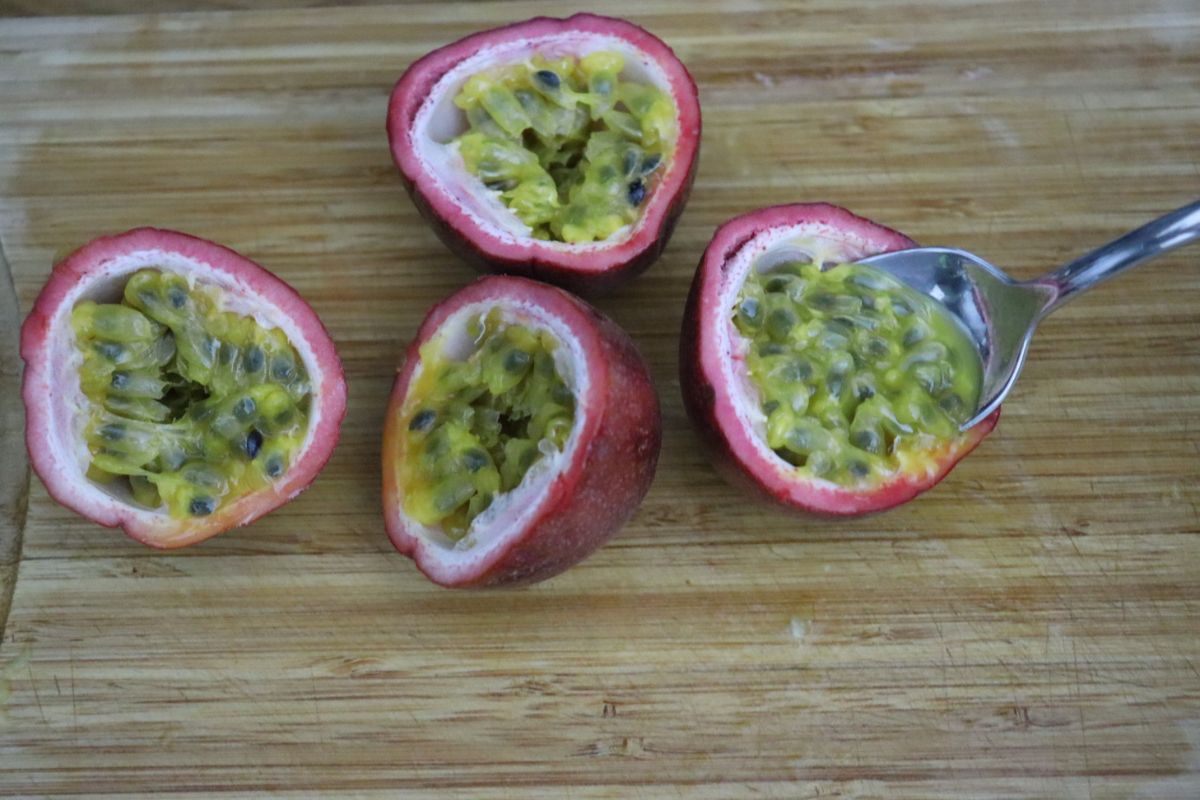 2 passion fruits cut in half and a spoon scraping the inside of one of them.