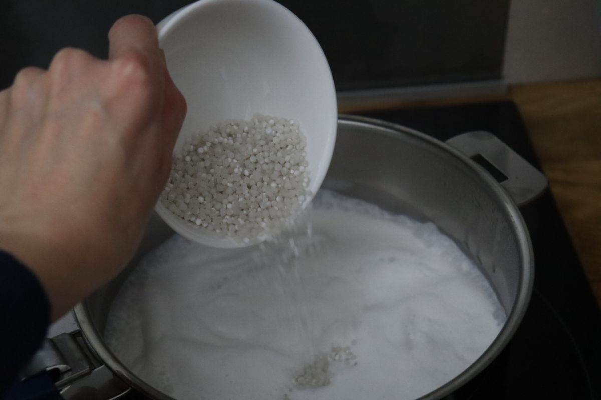 tapioca pearls being poured in the saucepan full of coconut milk