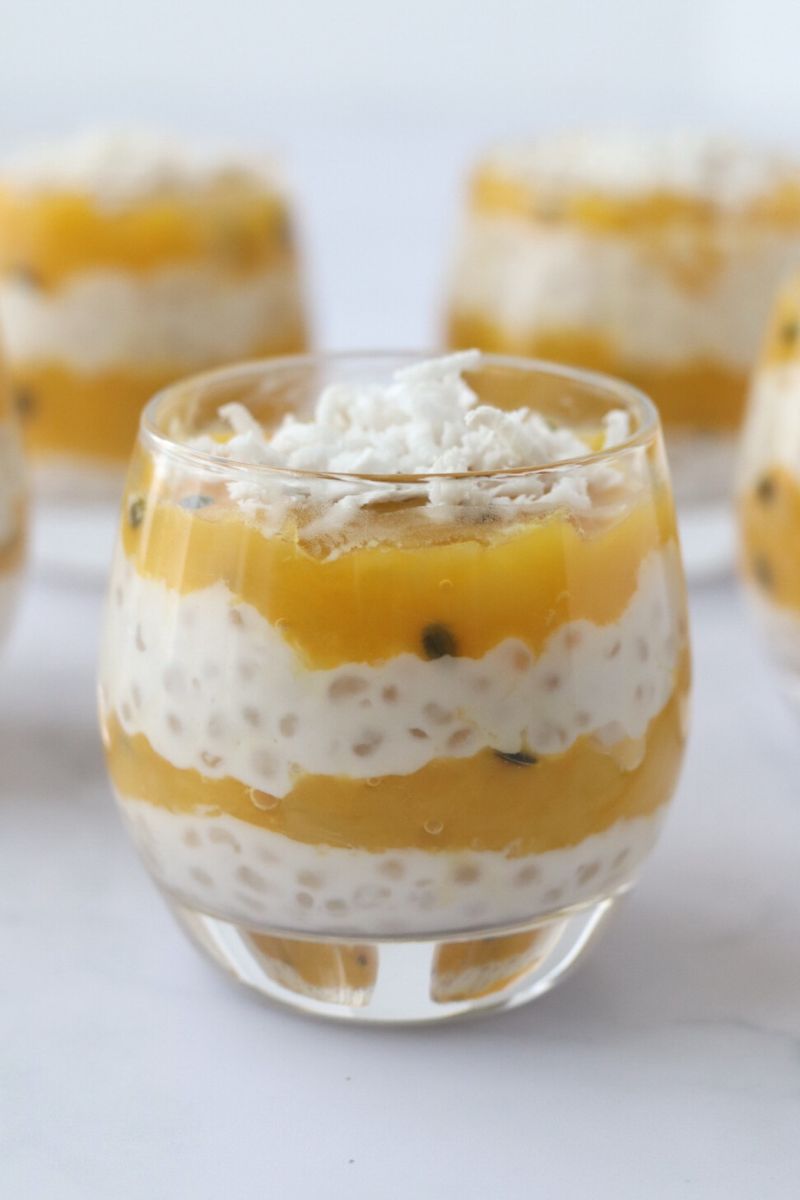 a glass full of layered mango tapioca pudding topped with grated coconut and 4 other glasses in the background