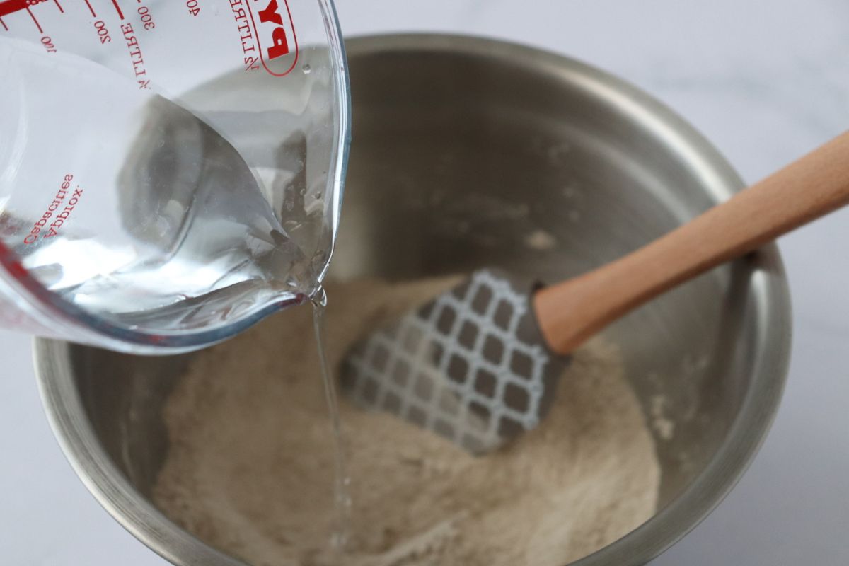 water being poured into a mixing bowl that contains buckwheat flour