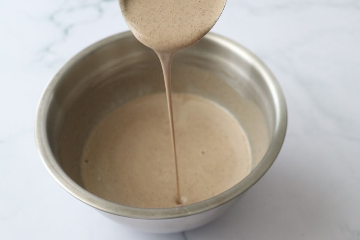 a smooth watery buckwheat batter pouring from a ladle in a bowl