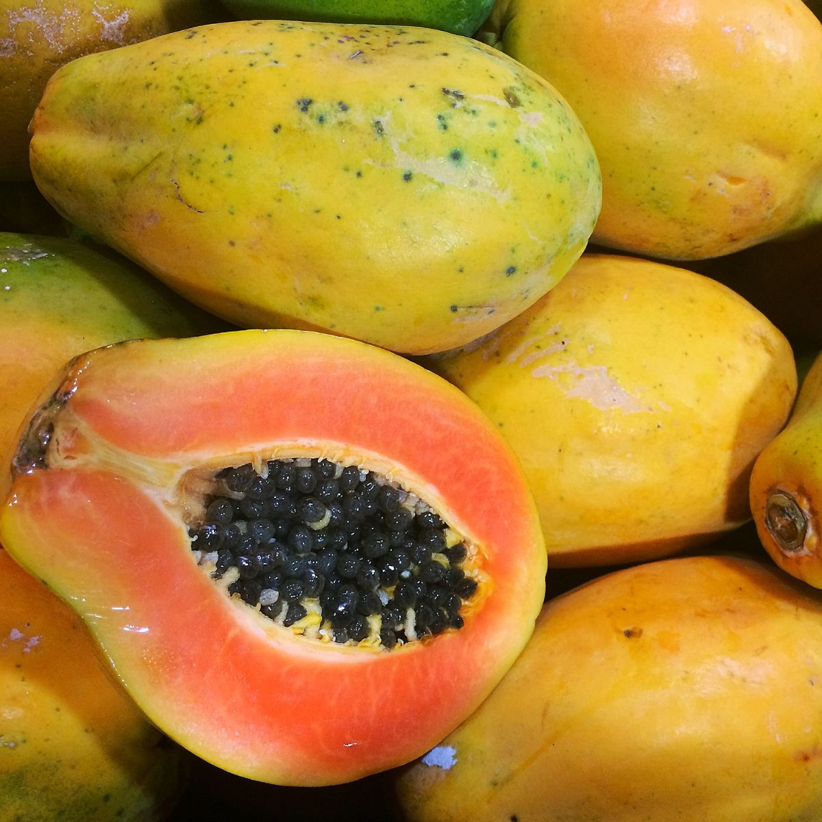 Half a yellow papaya perched on a bunch of papayas.