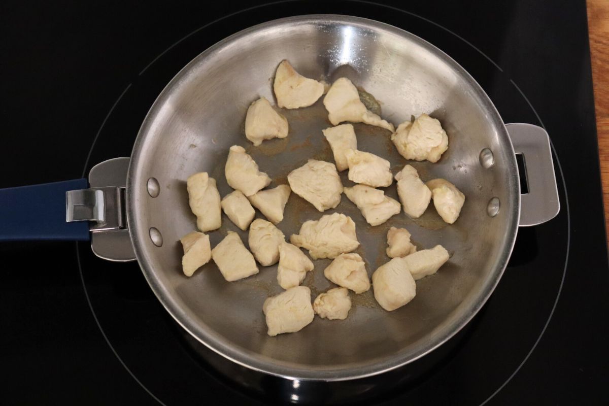 Cubes of chicken cooking in a frying pan on the stove. 