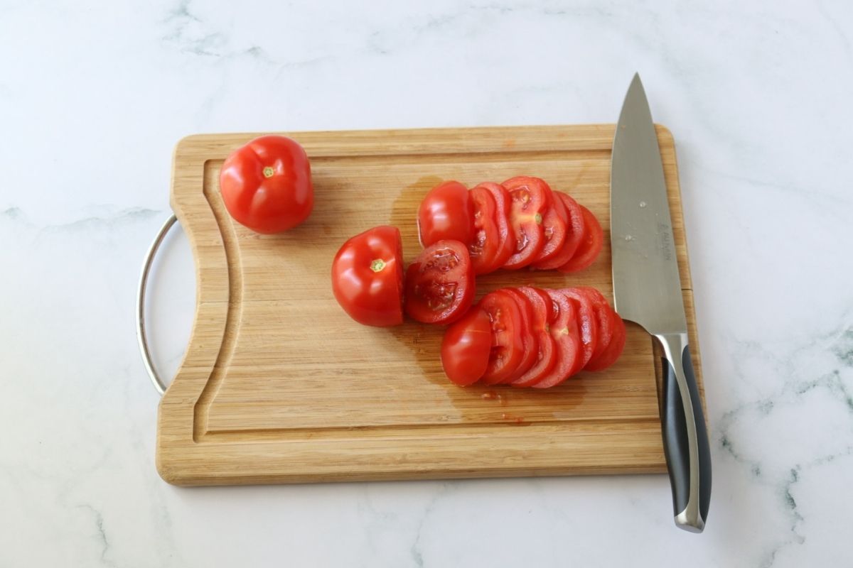 Some tomatoes being sliced on a wooden cutting board.