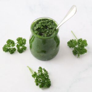 A jar full of parsley pesto and some curly parsley around it.