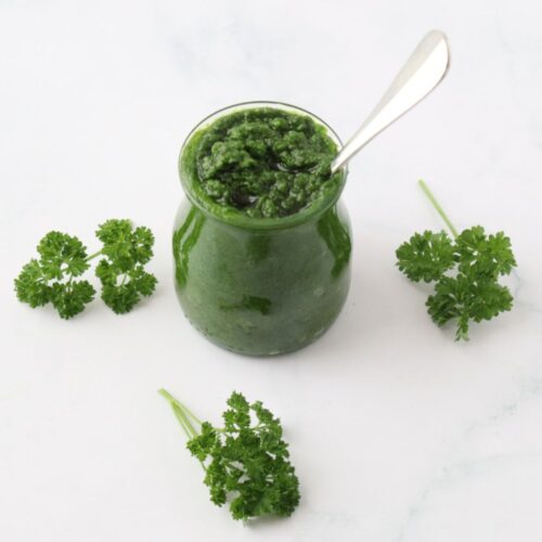 Un pot rempli de pesto de persil et des petits bouquets de persil tout au autour pour décorer.