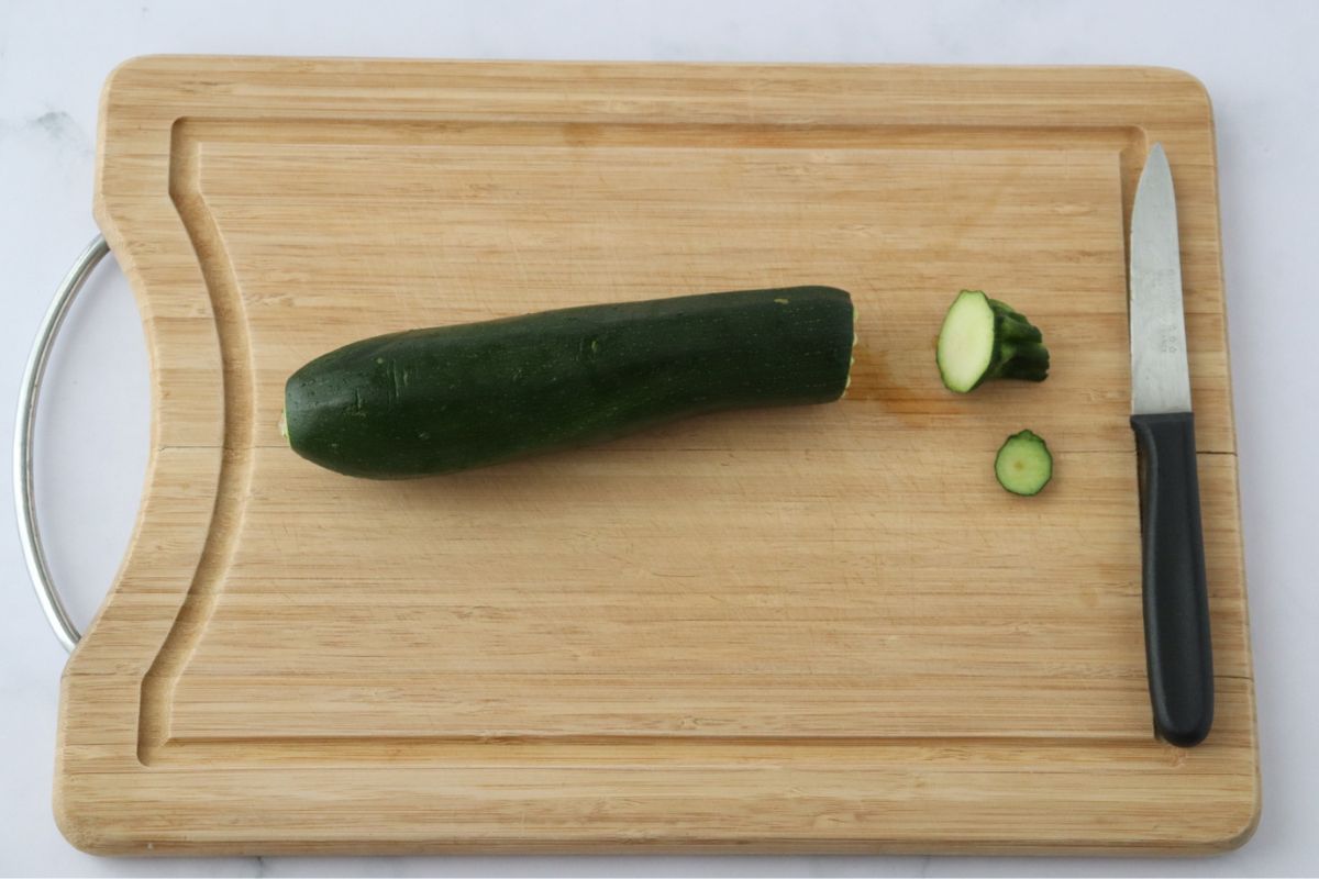 A zucchini on a wooden cutting board with the ends cut off.