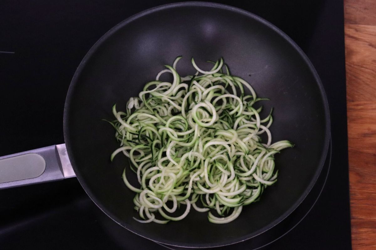 Zucchini noodles in a wok on the stove.