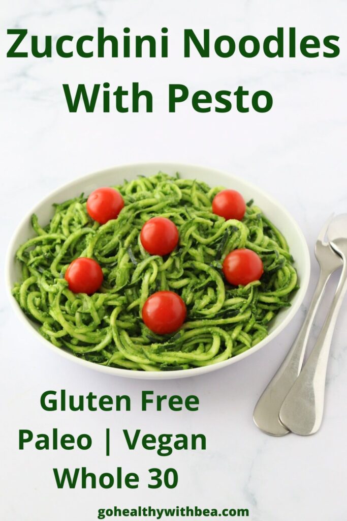 A plate full of zucchini noodles coated with pesto and some cherry tomatoes on top, a spoon and a fork on the side and a text overlay with the title.