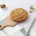 A gluten free yeast free focaccia on a wooden board, olives and herbs de Provence on the side.