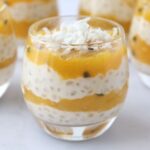 A glass full of layered mango tapioca pudding topped with grated coconut and 4 other glasses in the background.