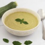 A bowl of cold zucchini soup and basil leaves on top to decorate.
