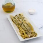 Leek salad on a white rectangular plate a bottle of olive oil and sea salt in a small bowl.