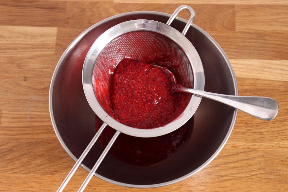 Straining the raspberry sauce with a fine-mesh strainer to remove the seeds.