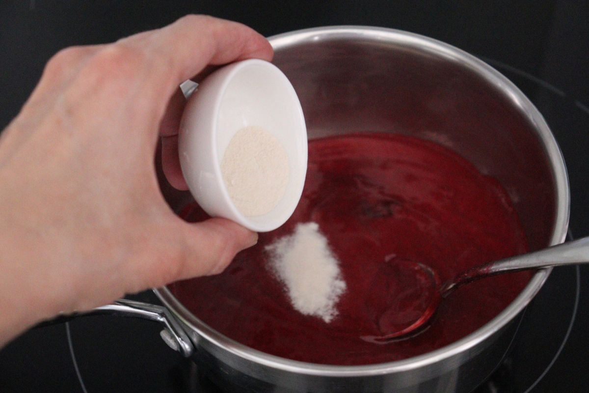 Adding the agar agar to the saucepan containing the strained raspberry sauce.