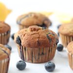 6 lemon blueberry muffins surrounded by fresh blueberries and lemons around them.