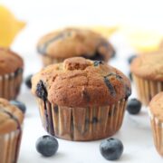 6 lemon blueberry muffins surrounded by fresh blueberries and lemons around them.