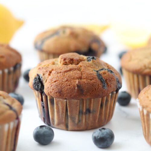 6 lemon blueberry muffins surrounded by fresh blueberries and lemons around them.