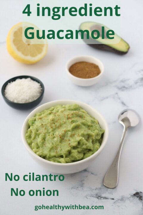 A white bowl full of guacamole, a spoon on the side, sea salt ground cumin half an avocado and half a lemon in the background.
