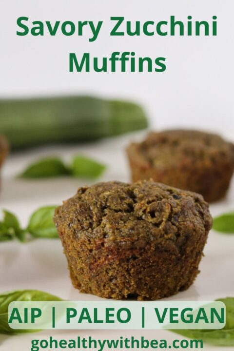 2 zucchini and pesto muffins basil leaves and a zucchini in the background.