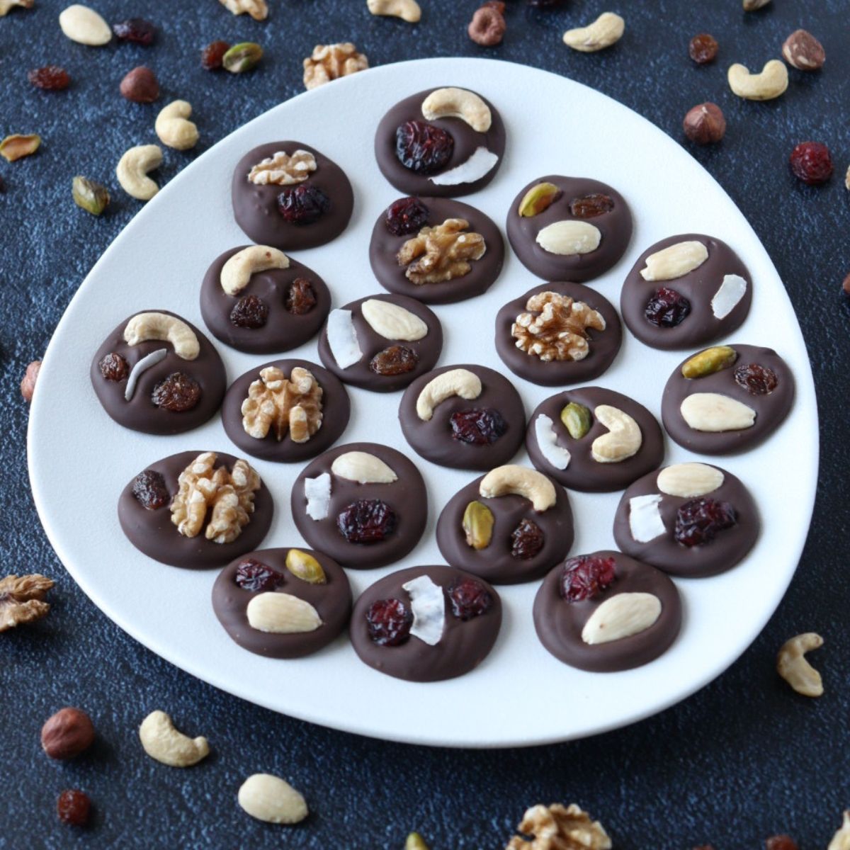 Une assiette recouverte de mendiants chocolat fruits secs et des fruits à coque et fruits secs tout autour pour décorer.