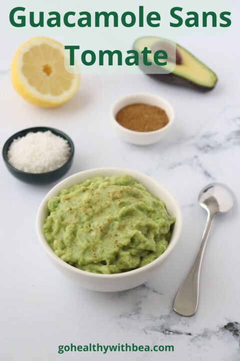 Un bol rempli de guacamole, une cuillère, du sel du cumin un demi citron et un demi avocat tout autour du bol.