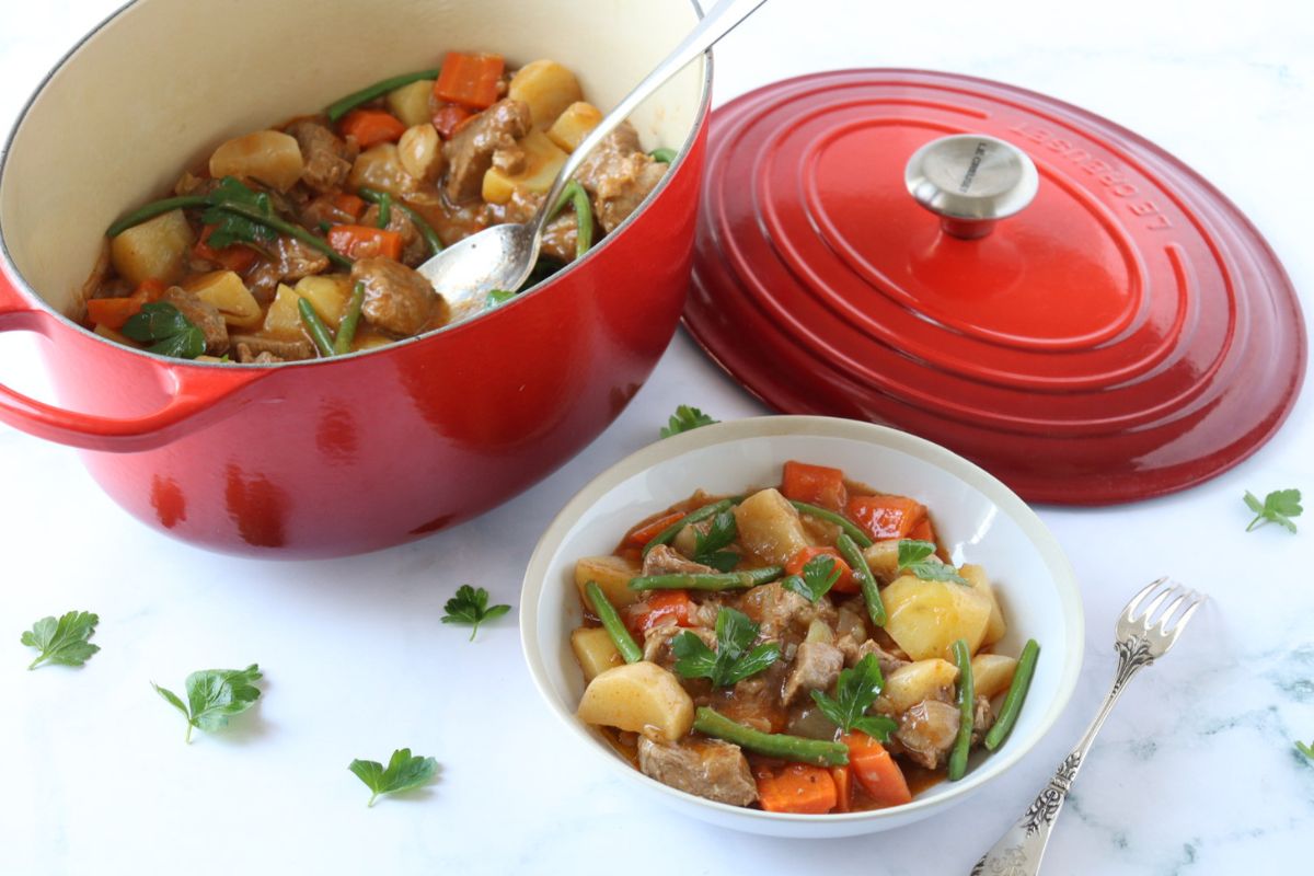 A plate of French Lamb Stew Navarin next to the cast iron Dutch oven where it was cooked.