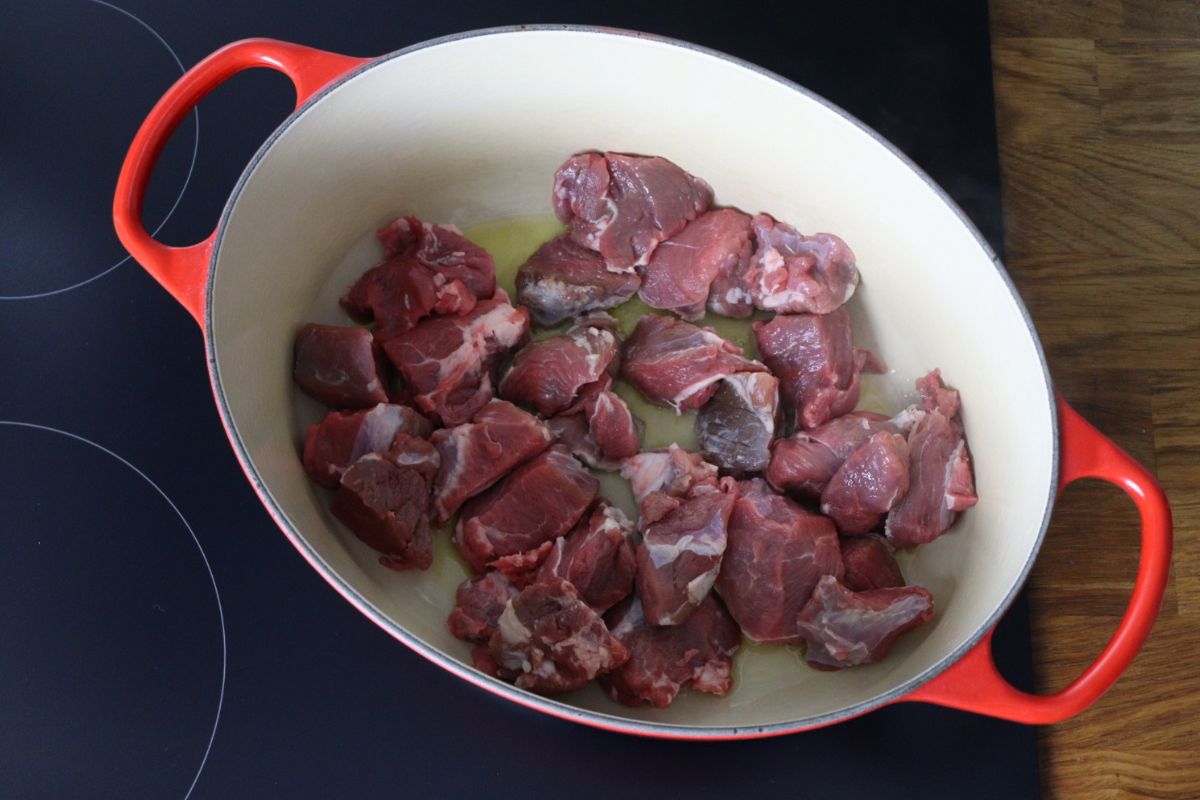 Lamb meat cooking in olive oil in a Dutch oven.