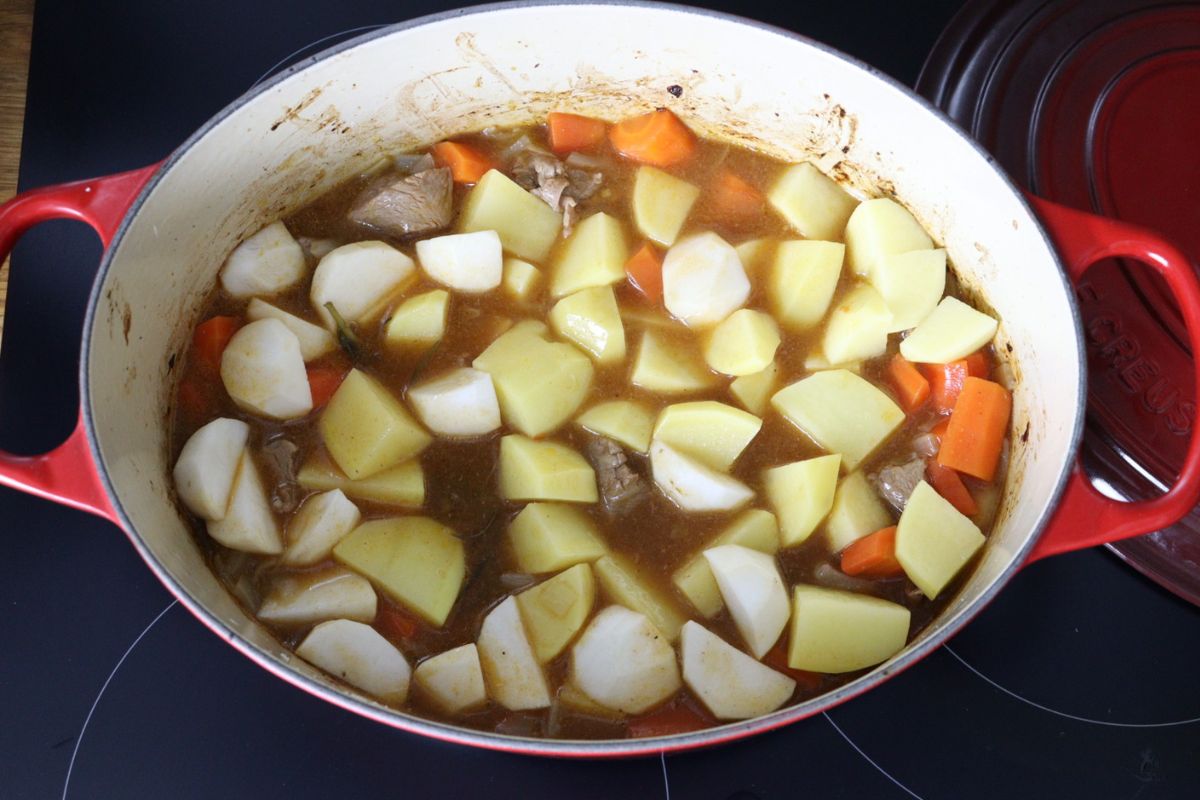 Dutch oven filled with lamb stew then topped with potatoes and turnips.