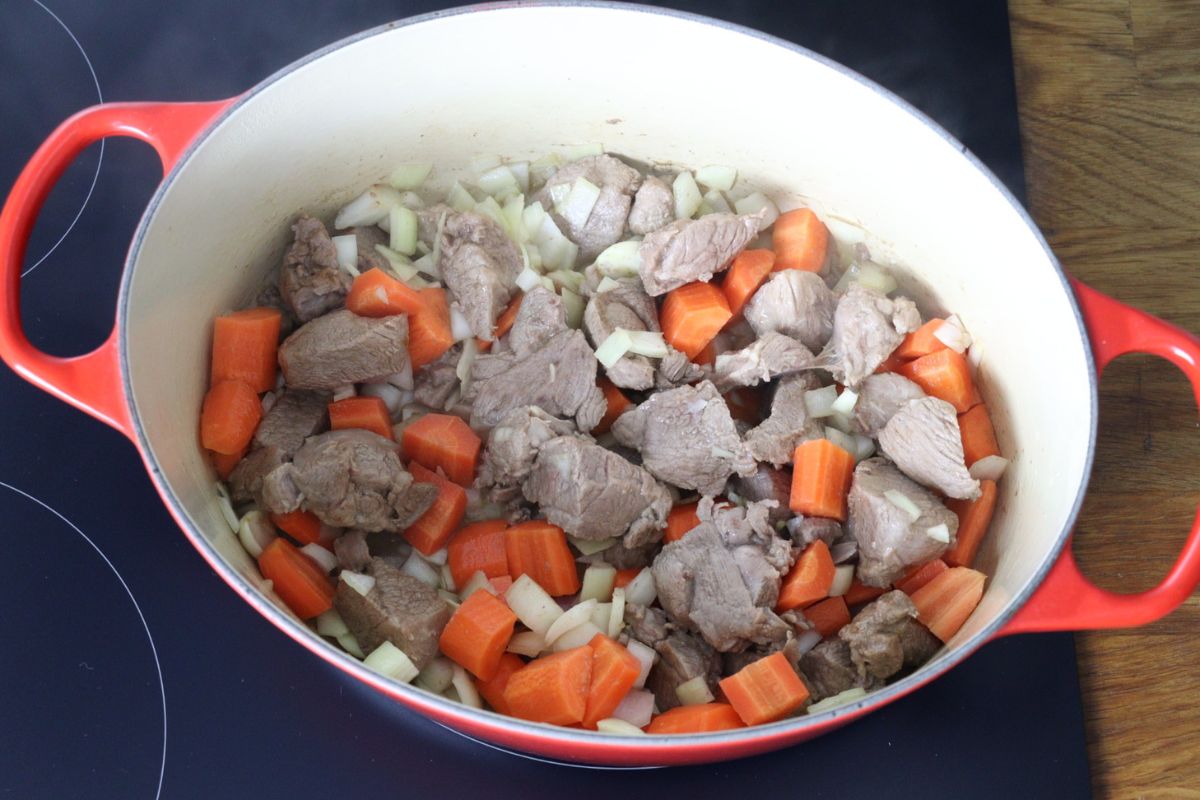 Lamb meat cooking in a Dutch oven with carrots, onion and garlic.