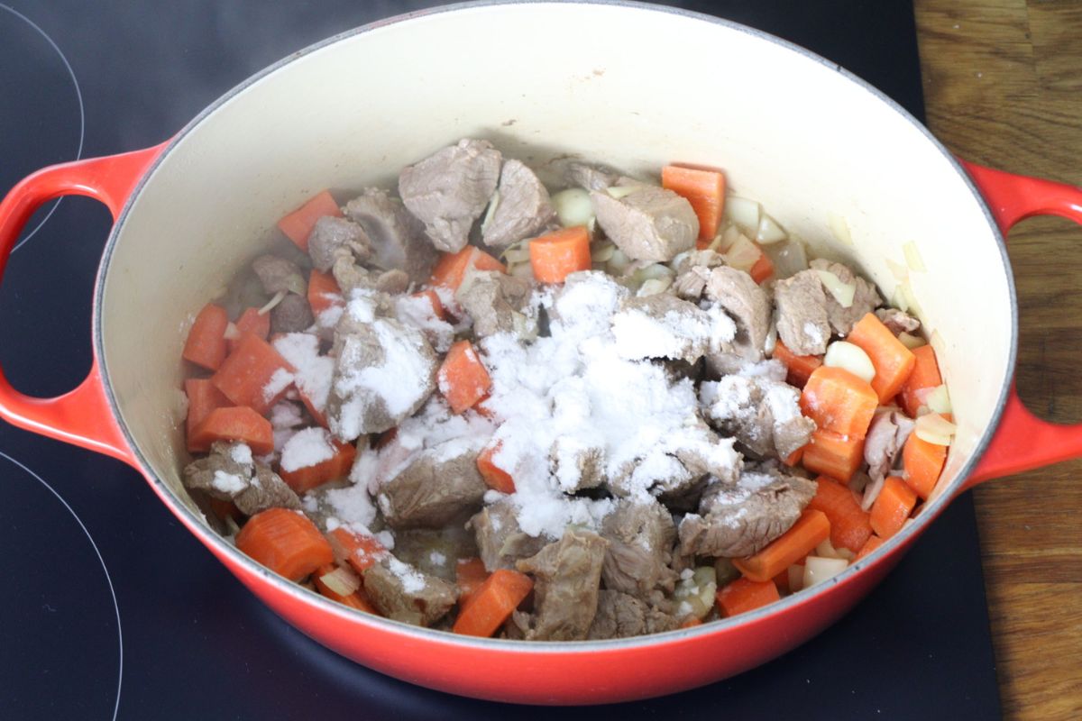 Lamb meat cooking in a Dutch oven with carrots, onion, garlic and arrowroot sprinkled on top.