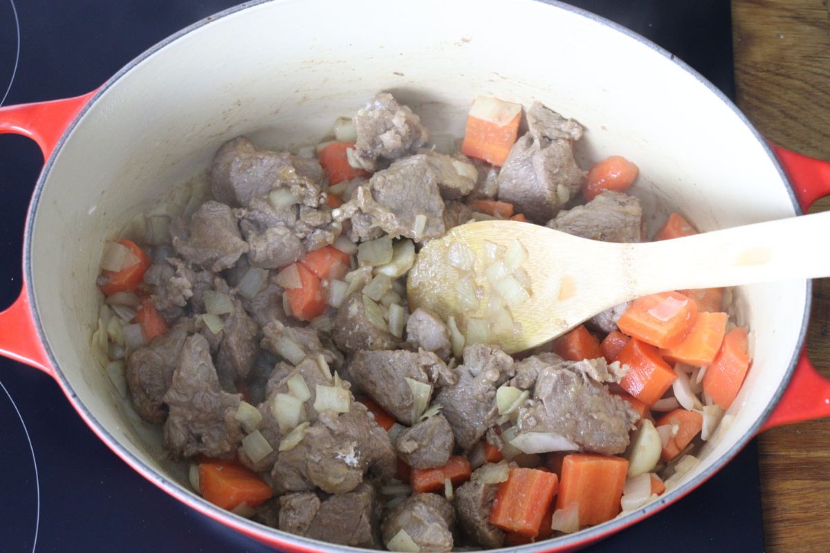 Lamb meat cooking in a Dutch oven with carrots, onion, garlic and arrowroot mixed in it.