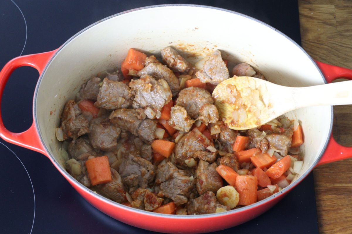 Lamb meat cooking in a Dutch oven with carrots, onion, garlic and arrowroot and tomato paste mixed in it.